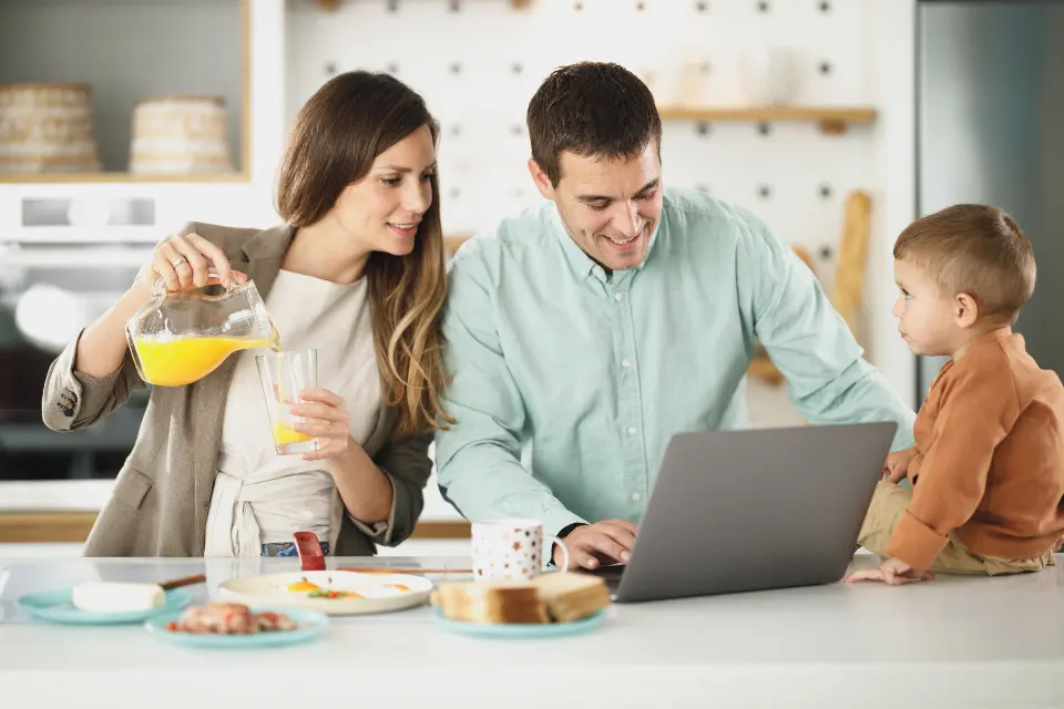Casal à mesa da cozinha com o filho, a tratar das contas no portátil