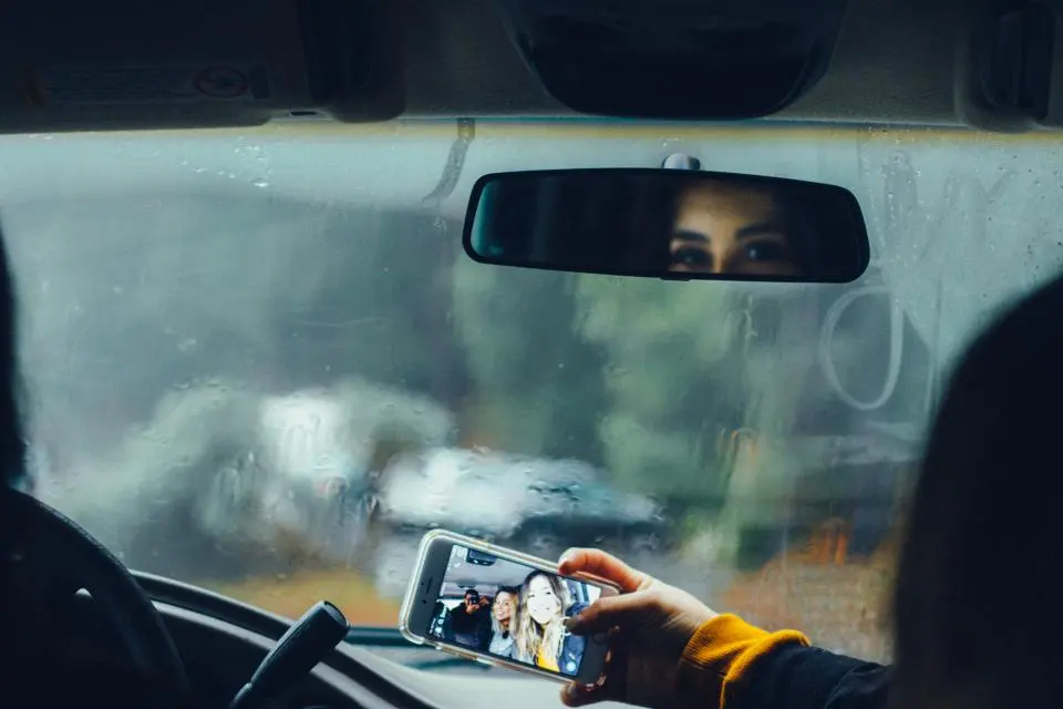 Condutora ao volante, vista pelo retrovisor num dia de chuva